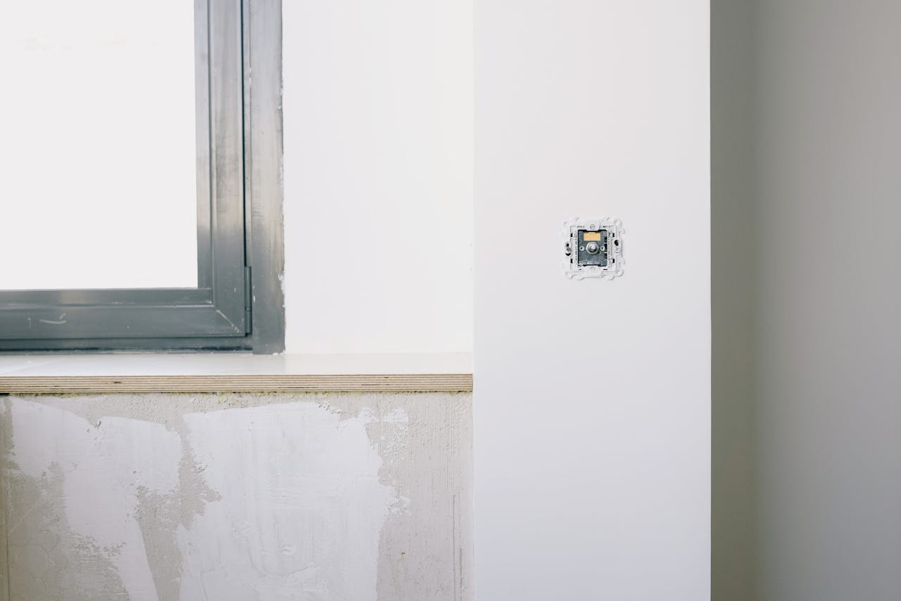 Repairs and installation of new electrical outlet on white wall near window in light apartment